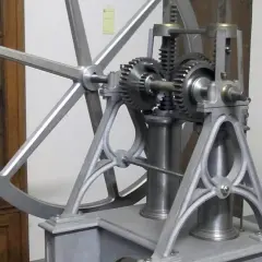 Mechanizm z kołem zamachowym i zębatkami, przypominający pierwszy silnik spalinowy.