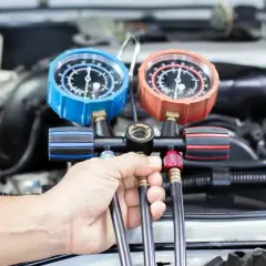 Ręka mechanika trzyma manometr do serwisu klimatyzacji samochodowej. Sprawdź nasz cennik usług.