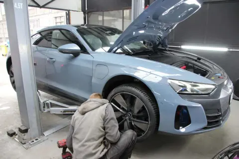 Mechanik przykręca koło w szarym samochodzie elektrycznym na podnośniku. Szybka odpowiedź na pytanie: ile trwa zmiana opon?