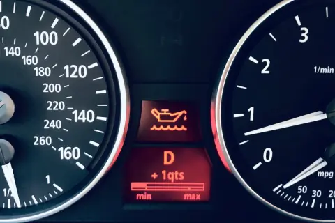 Żółta kontrolka oleju miga, wskazując na niski poziom płynu. Prędkościomierz pokazuje 0 km/h.