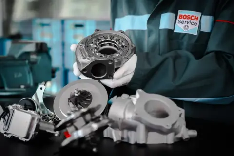 Mechanik w rękawiczkach prezentuje turbosprężarkę, kluczowy element dla wydajności silnika wolnossącego.