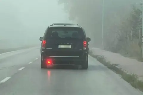 Ciemny van Dodge jedzie we mgle, włączone światła przeciwmgielne tylne poprawiają widoczność.