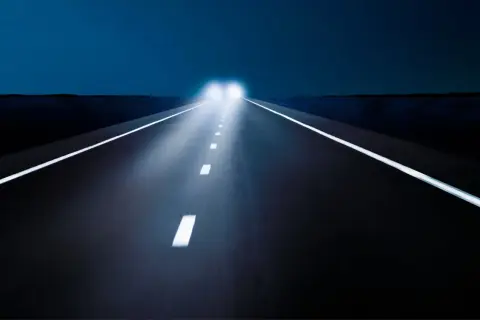 Nocna droga z jasnymi światłami mijania, które oświetlają białe linie.