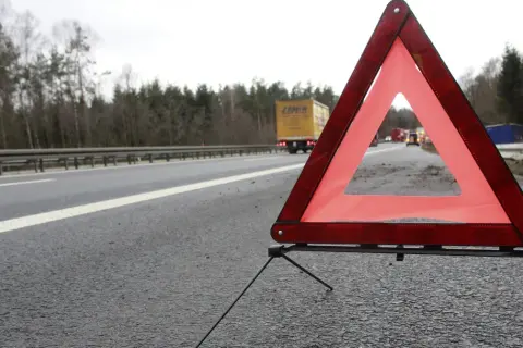 Czerwony trójkąt ostrzegawczy na poboczu drogi, sygnalizujący awarię. W tle ciężarówka i inne pojazdy.