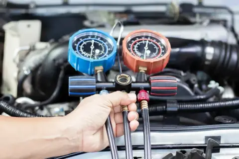 Ręka mechanika trzyma manometr do serwisu klimatyzacji samochodowej. Sprawdź nasz cennik usług.