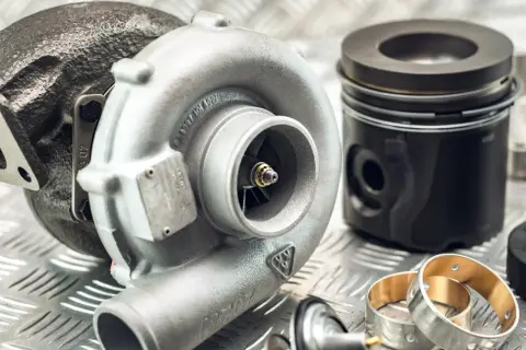 Turbosprężarka i tłok marki Kolbenschmidt na metalowej powierzchni.