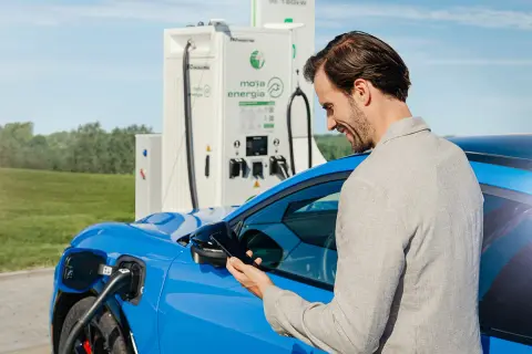 Mężczyzna sprawdza na telefonie koszt ładowania samochodu elektrycznego przy stacji Moja Energia.