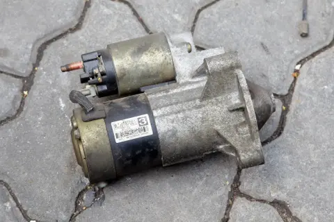 Dwa zużyte rozruszniki w aucie leżą na chodniku. Jeden ma naklejkę z napisem "MITSUBISHI JAPON".
