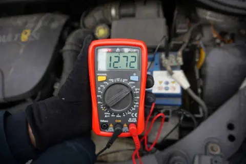 Multimetr pokazuje 12.72V, co może oznaczać brak ładowania akumulatora. Sprawdzanie stanu baterii w samochodzie.