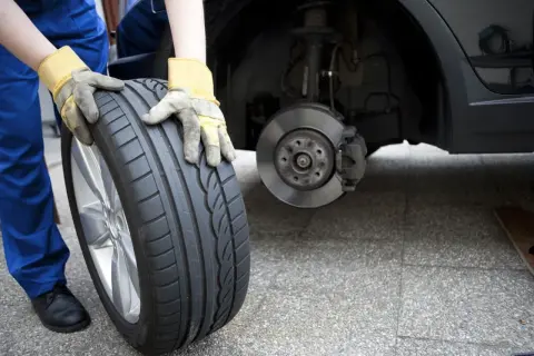 Mechanik w żółtych rękawicach trzyma nowe opony, zastanawiając się, czy lepsze opony na przód czy tył zapewnią bezpieczeństwo.