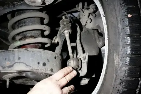 Dłoń mechanika wskazuje na zużyte tuleje stabilizatora w zawieszeniu samochodu.