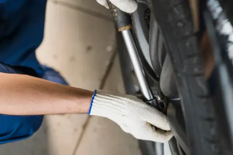Mechanik w białej rękawicy dokręca śruby koła kluczem dynamometrycznym, dbając o odpowiednią siłę dokręcania kół w samochodzie.