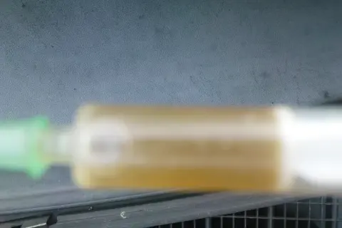 Strzykawka z żółtym płynem chłodniczym na tle deski rozdzielczej.