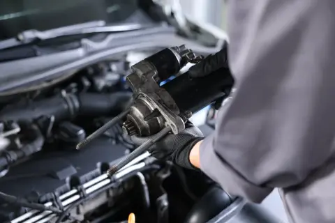 Mechanik w rękawiczkach trzyma rozrusznik. Zastanawiasz się, ile kosztuje wymiana rozrusznika?
