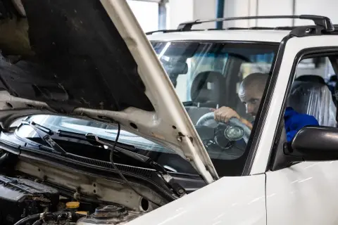 Mechanik sprawdza silnik białego auta. Czy to vaico co to za firma?