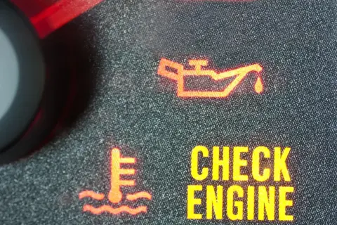 Czerwona kontrolka oleju świeci się, sygnalizując problem. Obok widać ikonę termometru i napis "CHECK ENGINE".