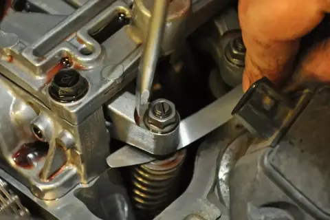 Mechanik reguluje zawory w silniku, używając śrubokręta i szczelinomierza.