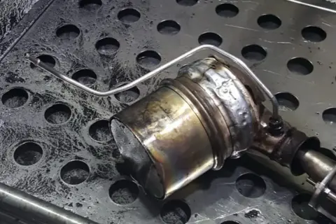Metalowy element układu wydechowego z widocznymi śladami zużycia i zabrudzeń.
