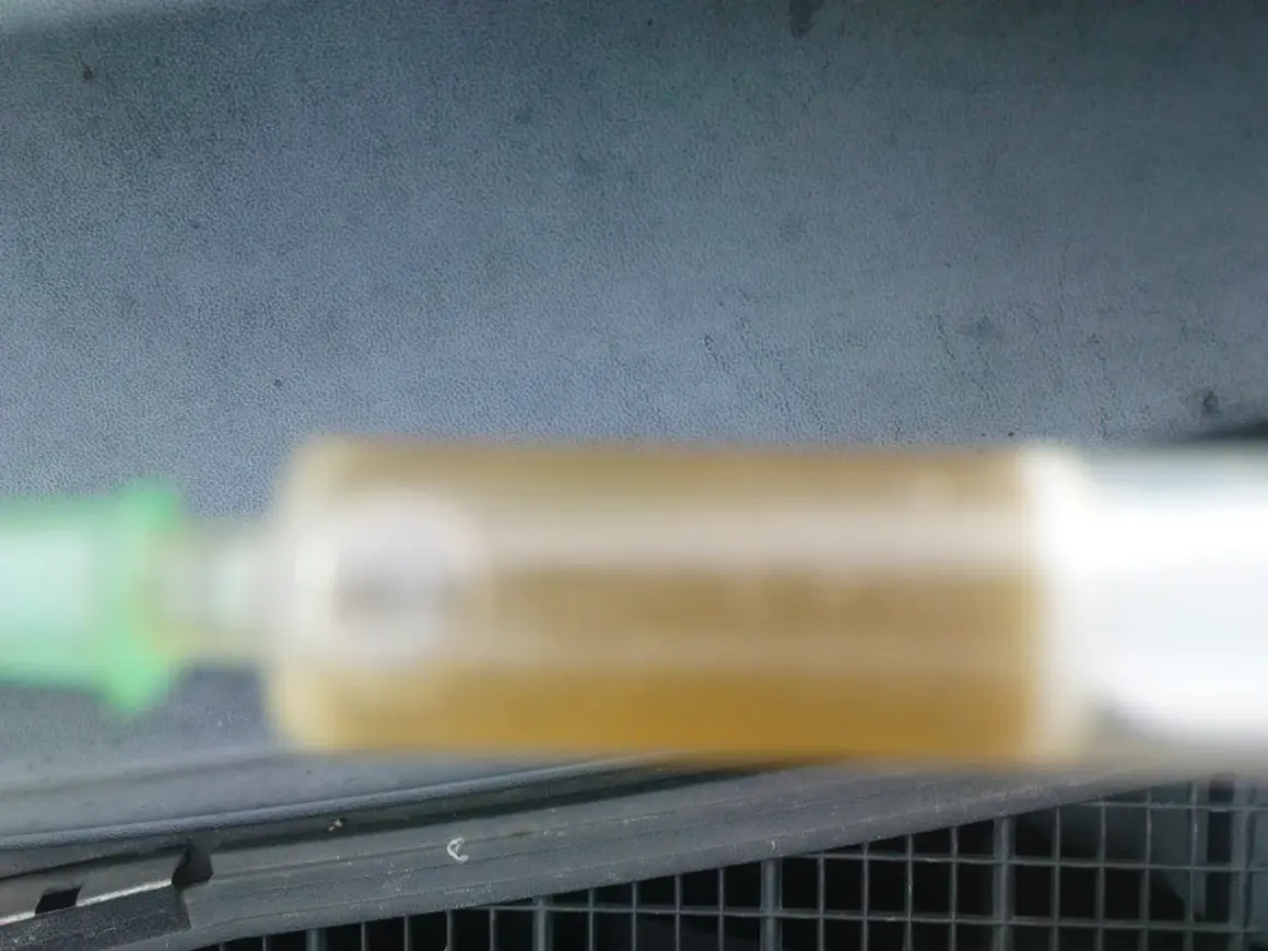 Strzykawka z żółtym płynem chłodniczym na tle deski rozdzielczej.