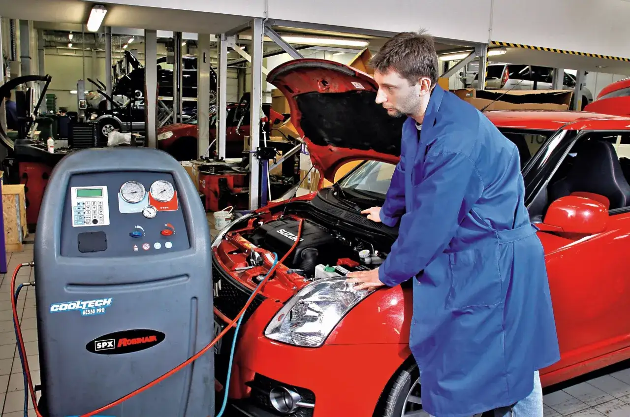 Mechanik sprawdza, ile kosztuje nabicie klimatyzacji w czerwonym Suzuki. Urządzenie Cooltech AC550 PRO jest podłączone do silnika.