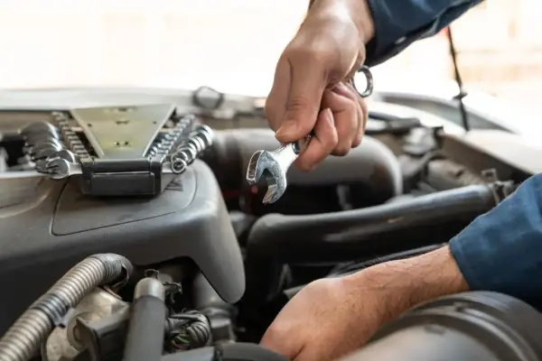Mechanik dokonuje wymiany sprężarki klimatyzacji, używając klucza do odkręcenia śrub w silniku samochodu.