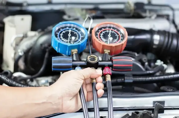 Ręka mechanika trzyma manometr do serwisu klimatyzacji samochodowej. Sprawdź nasz cennik usług.