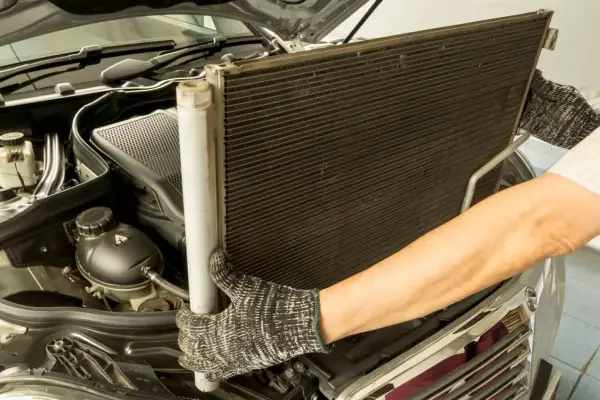 Mechanik wyjmuje chłodnicę klimatyzacji. Sprawdź wymiana chłodnicy klimatyzacji cena.