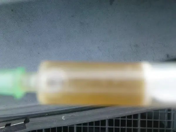 Strzykawka z żółtym płynem chłodniczym na tle deski rozdzielczej.